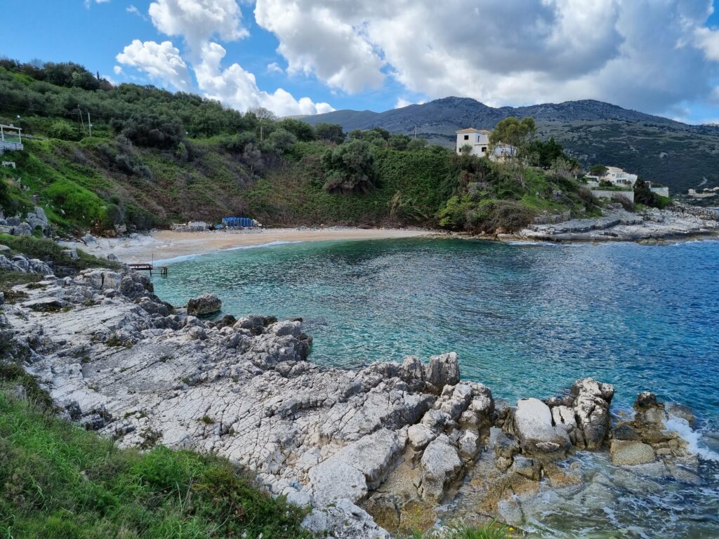 Urokliwa zatoczka z piaszczystą plażą, zielonym wzgórzem i turkusową wodą na Korfu