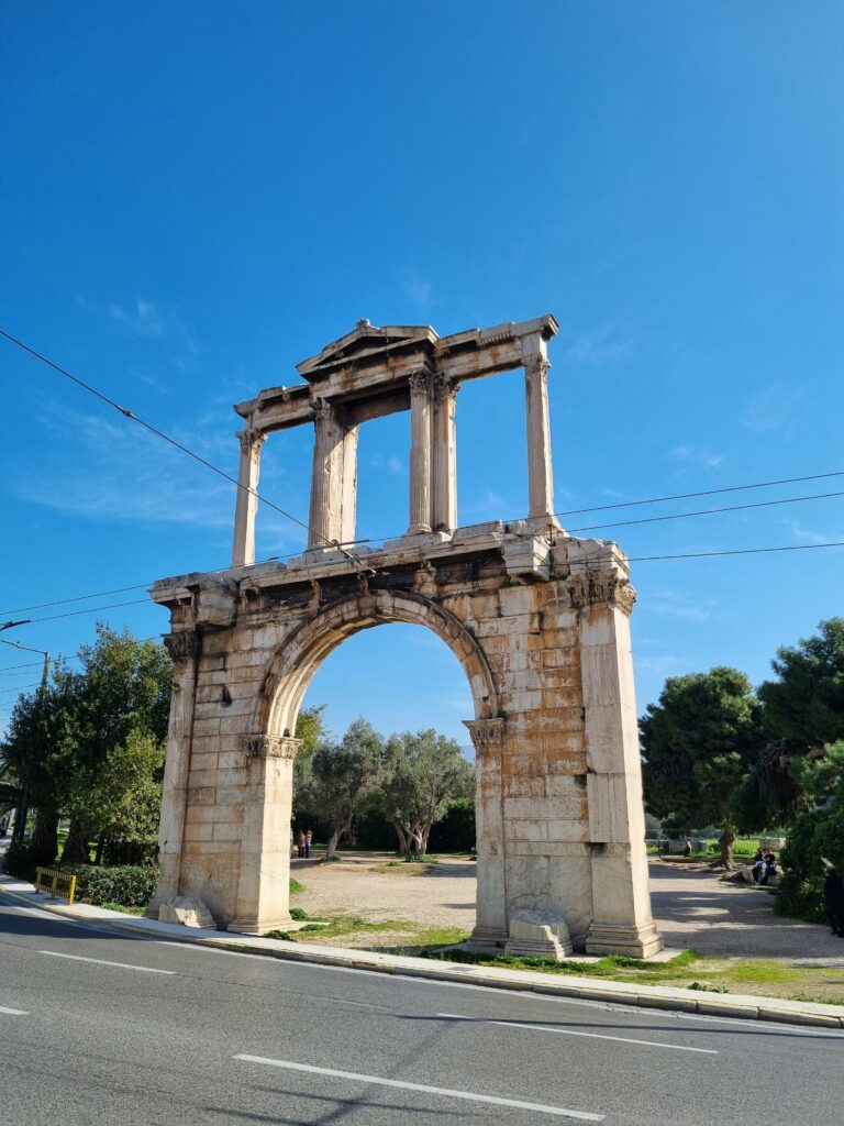 Monumentalny Łuk Hadriana w Atenach, z trzema łukowymi przejściami i kolumnami, stojący przy ulicy pod czystym błękitnym niebem.
