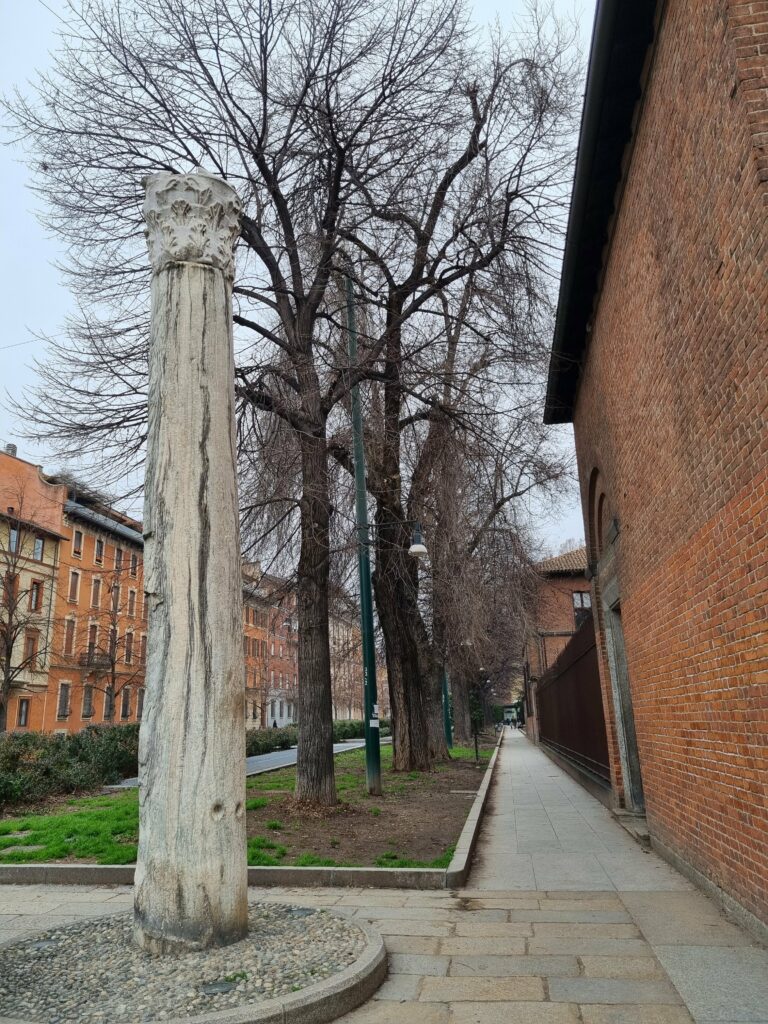 Marmurowa kolumna obok ceglanego muru w dzielnicy z drzewami i alejką