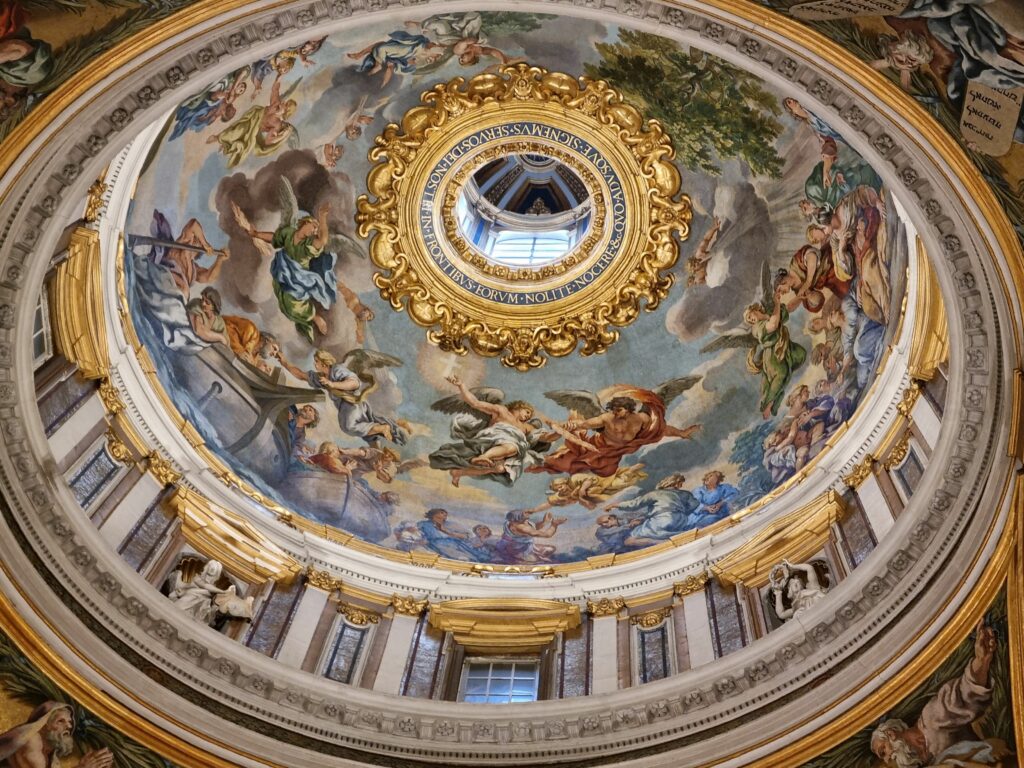 Wnętrze kopuły z bogatymi freskami przedstawiającymi sceny biblijne i postacie aniołów, otoczone złotymi zdobieniami i architektonicznymi detalami.