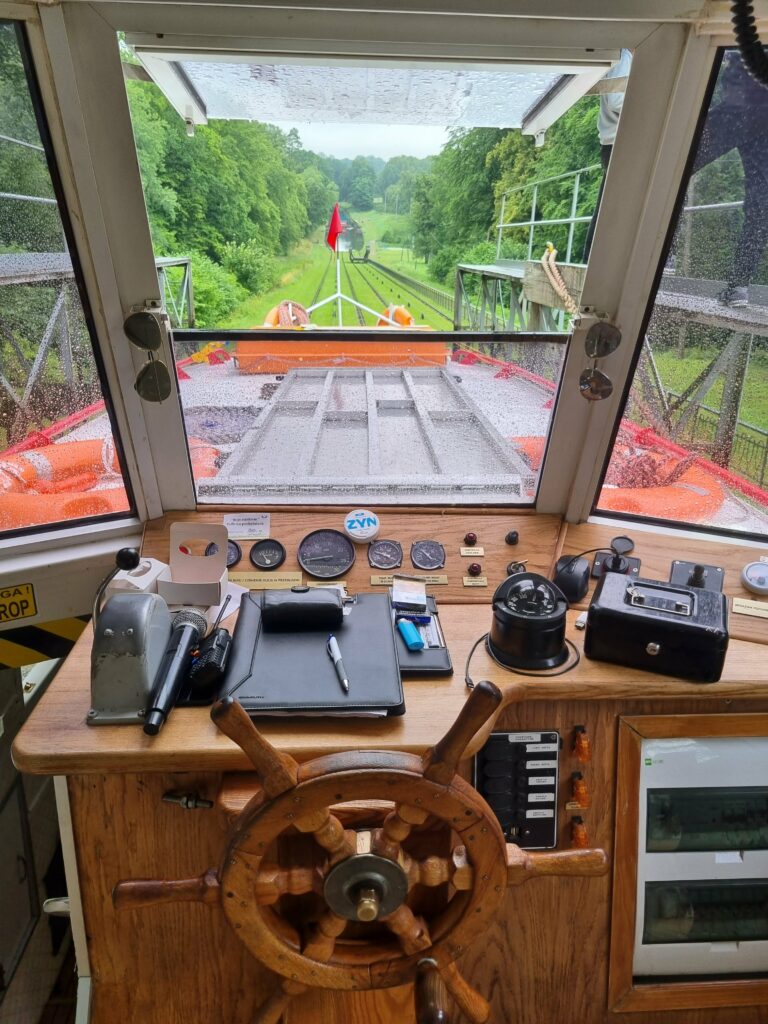 Kokpit statku na Kanale Elbląskim z widokiem na zielone torowisko pochylni i czerwona flaga.
