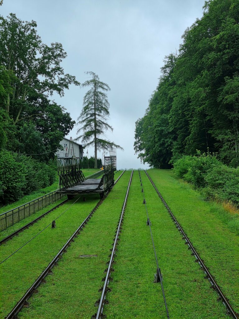 Zielone torowisko pochylni Kanału Elbląskiego z wózkiem transportowym w oddali.