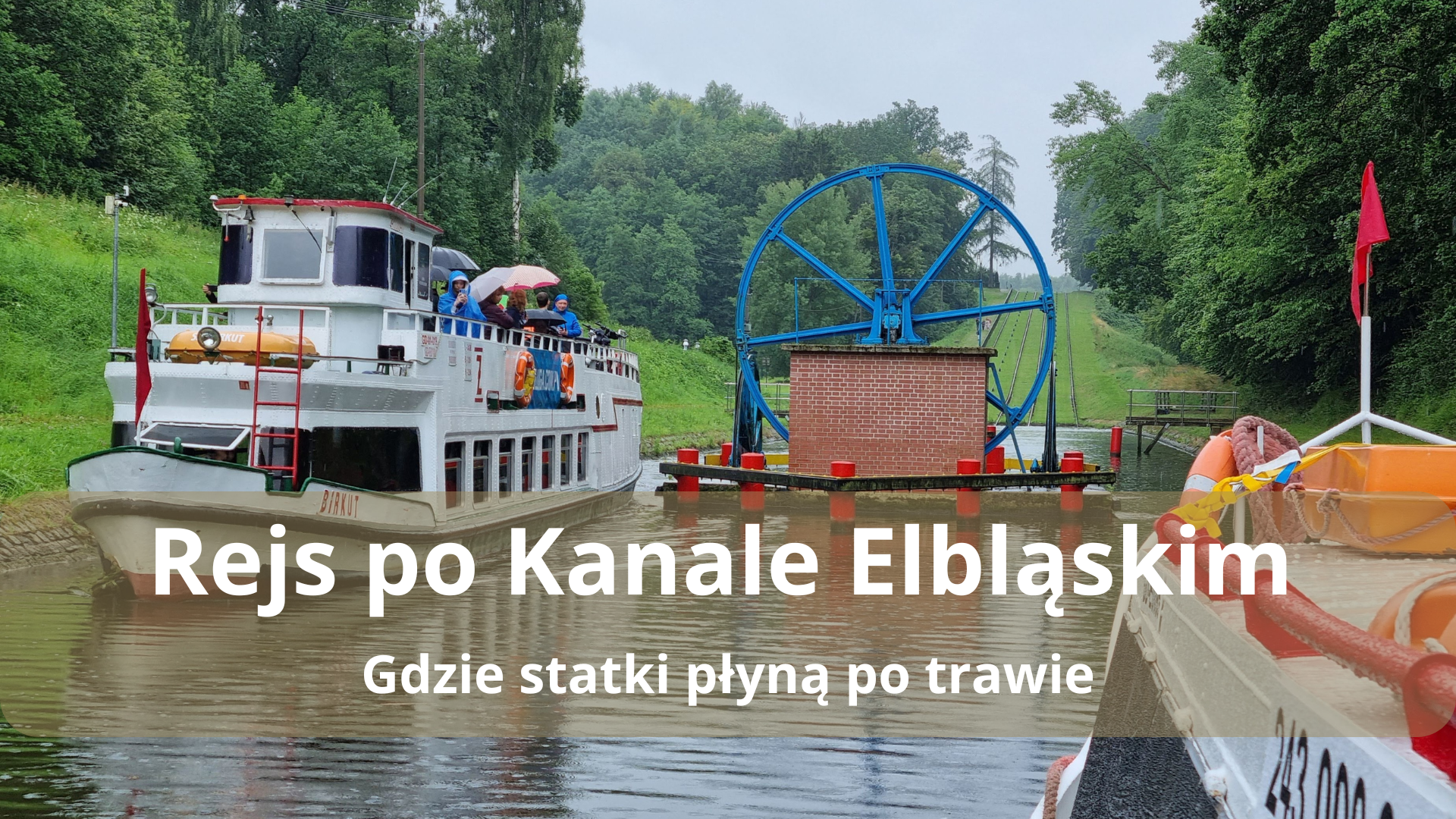 Statek na Kanale Elbląskim z niebieskim kołem mechanizmu pochylni w tle.