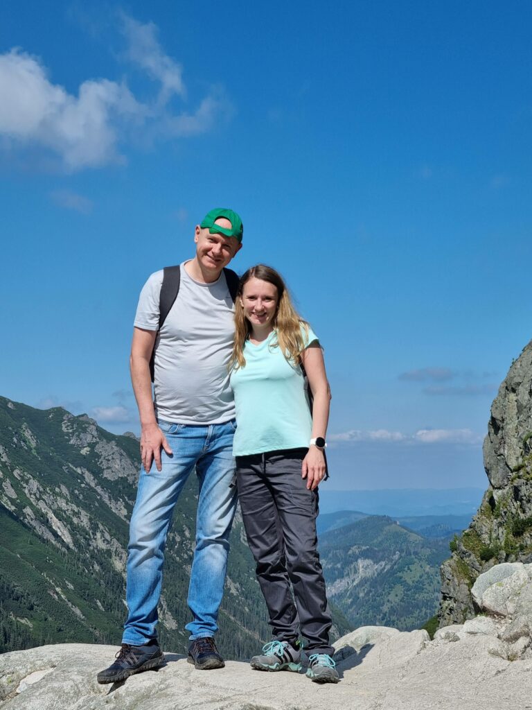 Para turystów pozująca na szczycie skalnej półki, z widokiem na tatrzańskie góry.