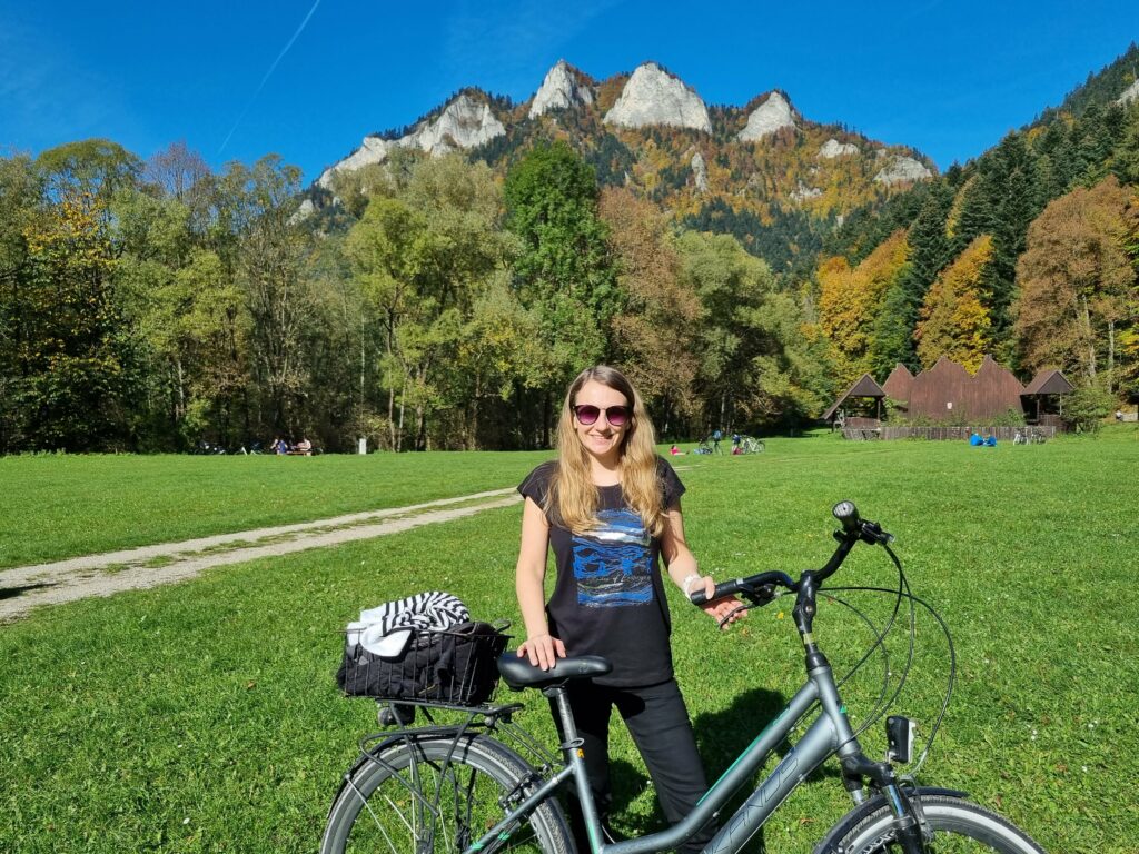 Uśmiechnięta kobieta na rowerze, z widokiem na Trzy Korony w Pieninach.
