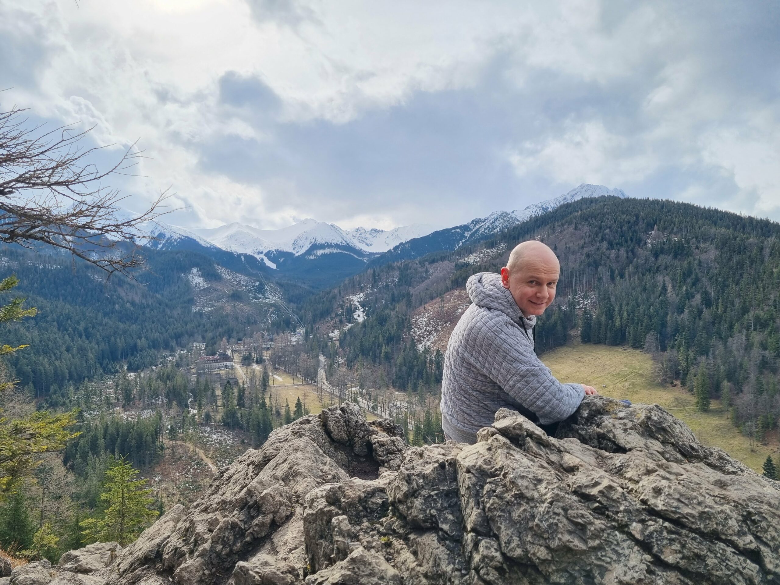 Szczęśliwy turysta siedzący na skalnej grani Nosala, z widokiem na pasmo Giewontu i ośnieżone Tatry, w tle.