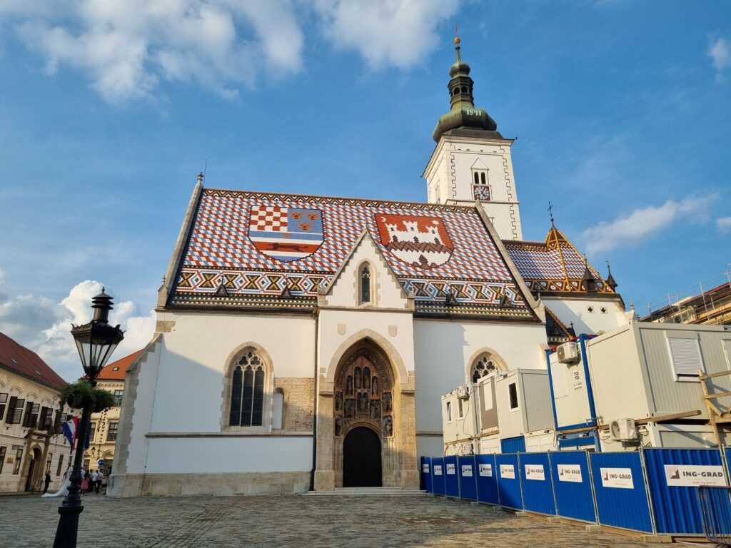 Kościół św. Marka na placu w Górnym Mieście w Zagrzebiu. Widoczny cały budynek z charakterystycznym dachem z herbami, wieżą i historyczną latarnią.