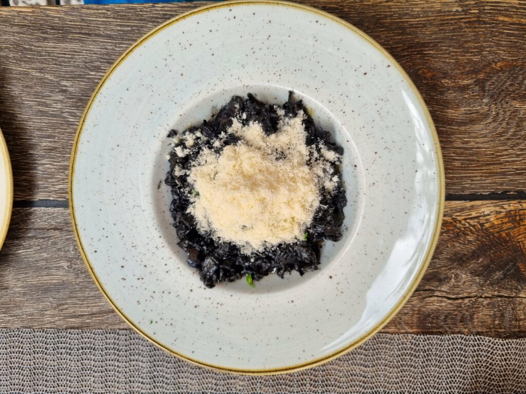 Czarne risotto, czyli crni rižot, w głębokim talerzu, posypane startym serem. Intensywne w smaku danie z owoców morza kuchni chorwackiej.