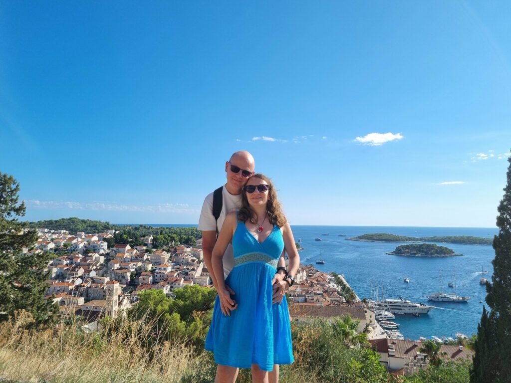 Para turystów (autorzy bloga) pozująca na tle zapierającej dech w piersiach panoramy miasta Hvar i Wysp Paklińskich. Widok z twierdzy Fortica (Španjola) w słoneczny dzień.