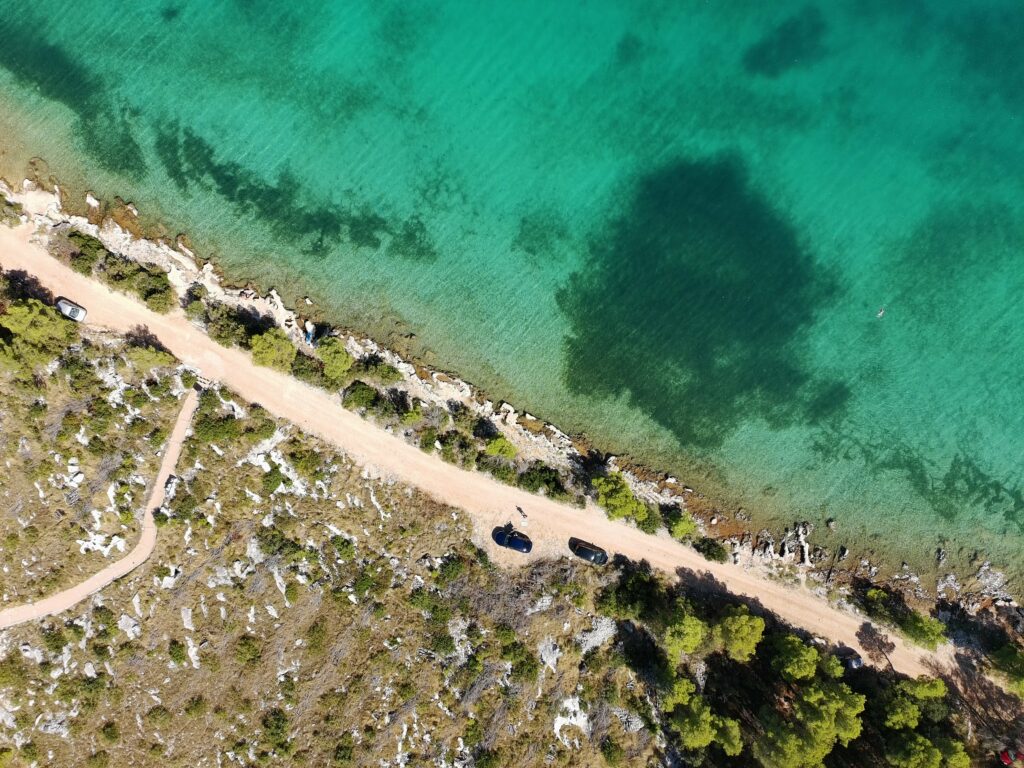 Widok z góry (z drona) na turkusową zatokę i wybrzeże przy Murze Oštrica. Samochody zaparkowane przy szutrowej drodze tuż obok plaży, to idealne miejsce na przystanek w trasie do Splitu.