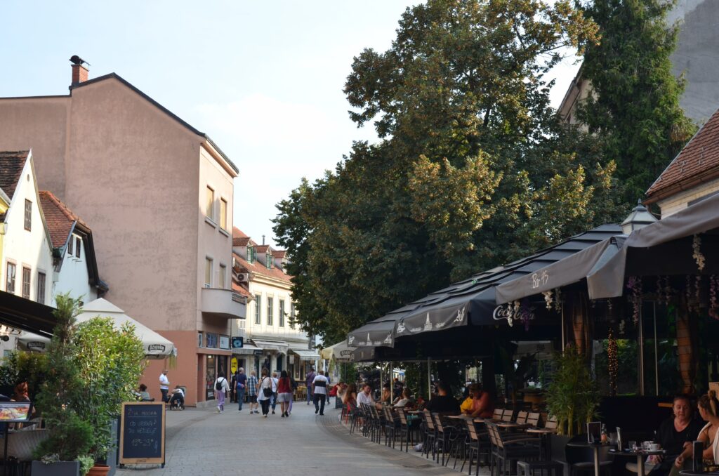 Tętniąca życiem ulica Tkalčićeva w Zagrzebiu, pełna kawiarni i restauracji z ogródkami, w których siedzą ludzie spacerujący po deptaku.
