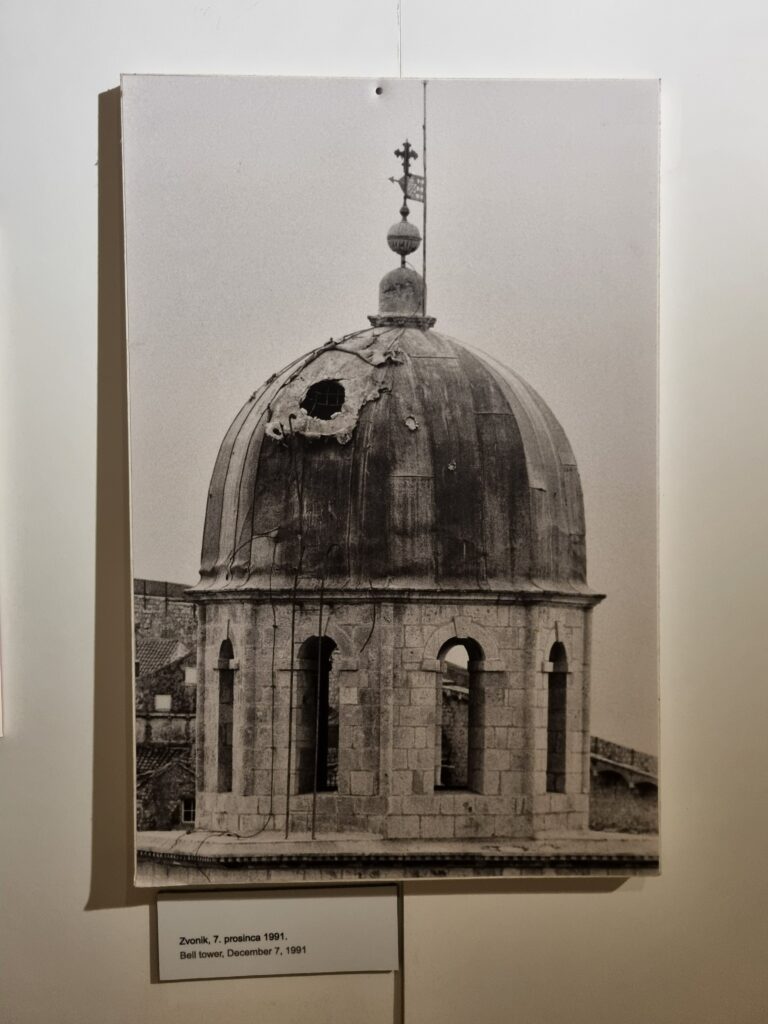 Czarno-białe zdjęcie uszkodzonej kopuły dzwonnicy w Dubrowniku po ostrzale w grudniu 1991 roku.