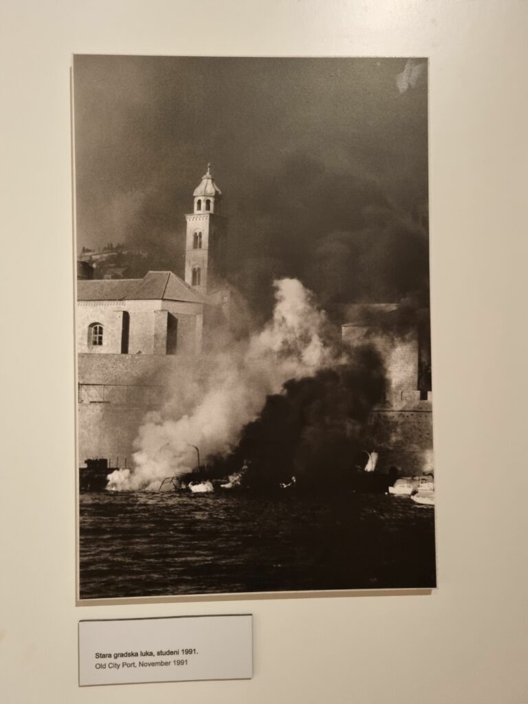 Archiwalne czarno-białe zdjęcie przedstawiające płonący Stary Port w Dubrowniku podczas oblężenia w listopadzie 1991 roku.
