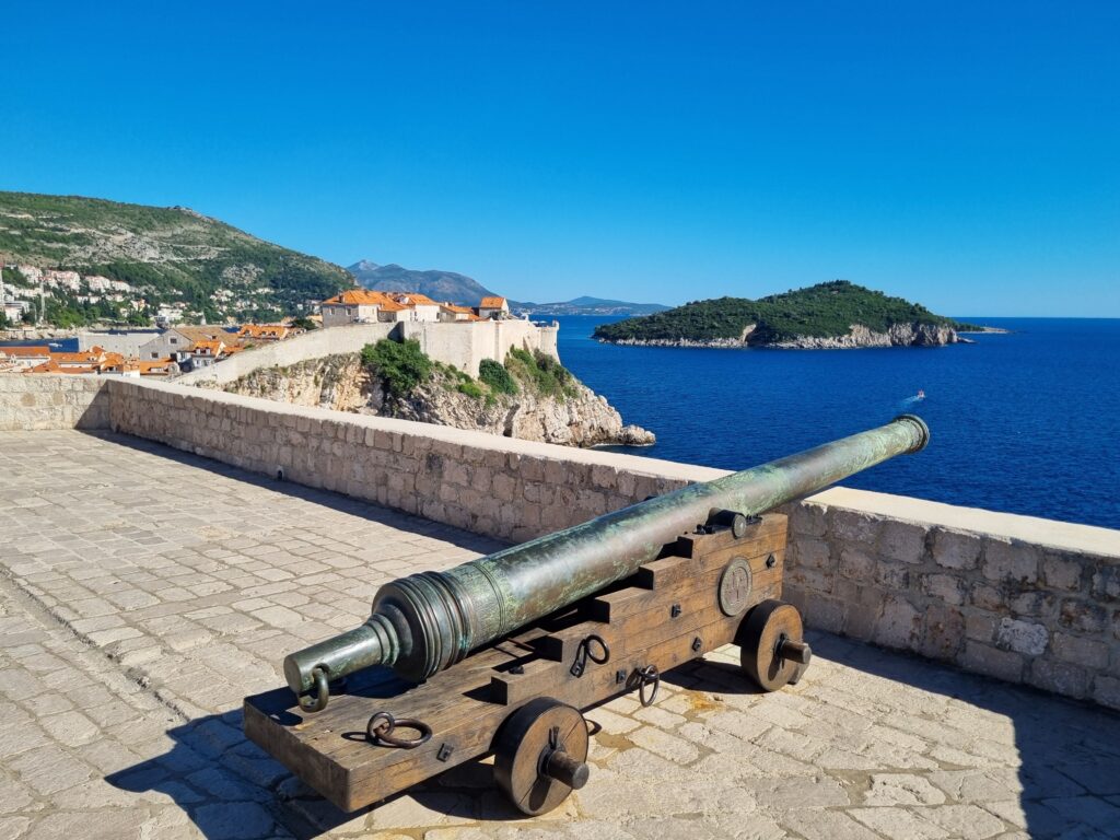 Zabytkowa armata z brązu na murach miejskich Dubrownika z widokiem na morze i wyspę Lokrum.