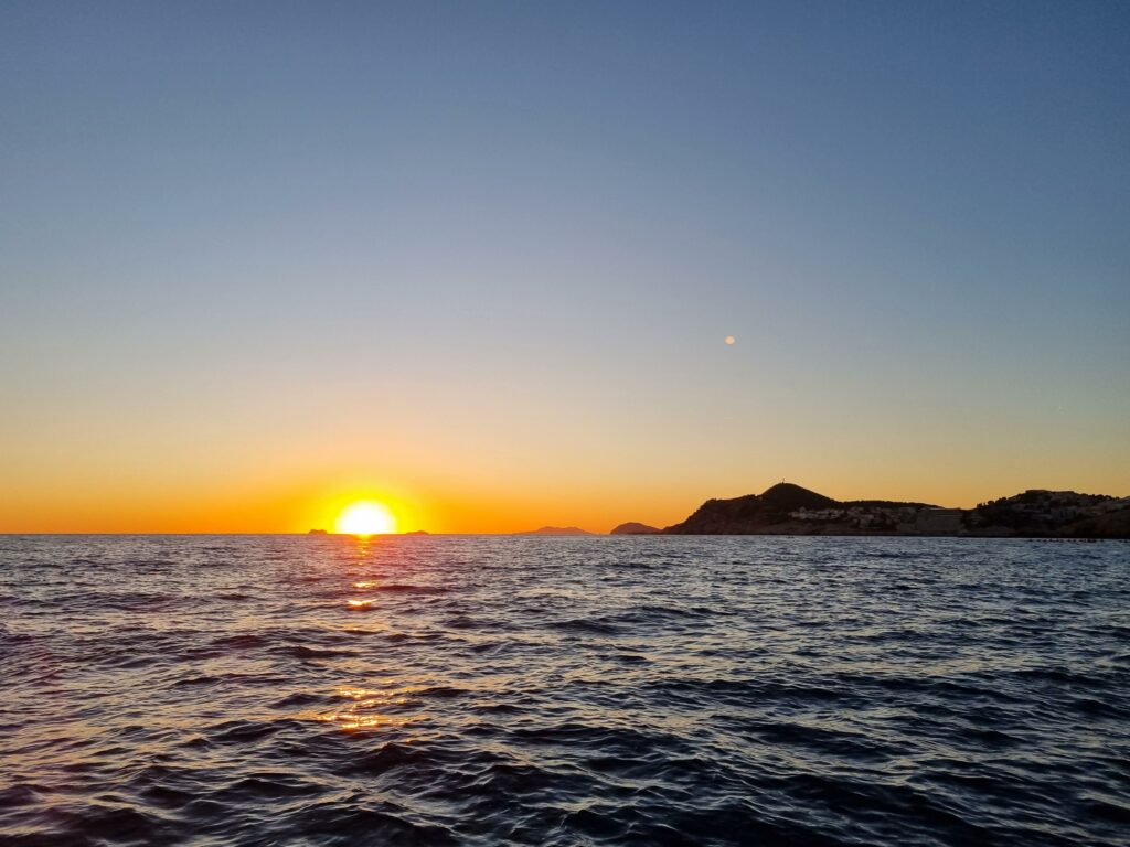 Zachód słońca nad murami Dubrownika widoczny podczas rejsu łodzią.