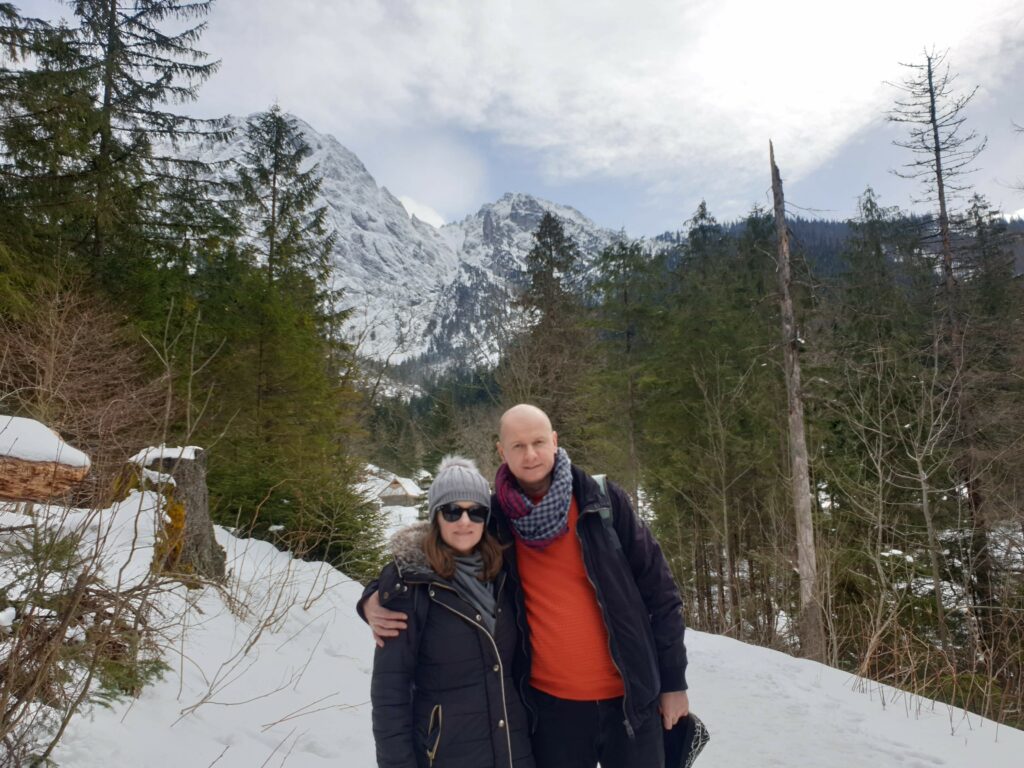 Uśmiechnięta para turystów stojąca na Polanie Strążyskiej z widokiem na szczyt Giewontu w tle