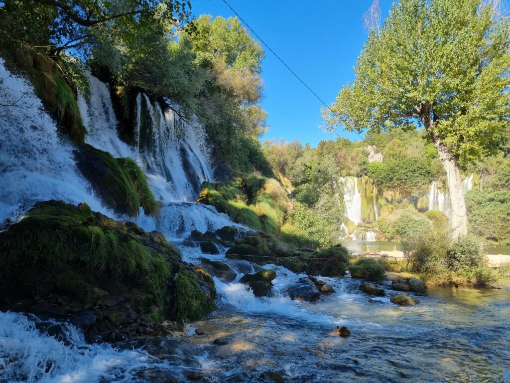 Szeroka panorama Wodospadów Kravica z kaskadami wody wpadającymi do szmaragdowego jeziora w Bośni i Hercegowinie.