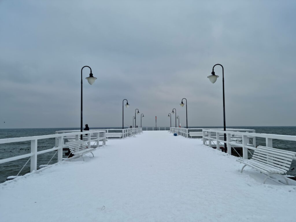 Symetryczny widok na ośnieżony pomost mola w Gdyni Orłowie z latarniami.