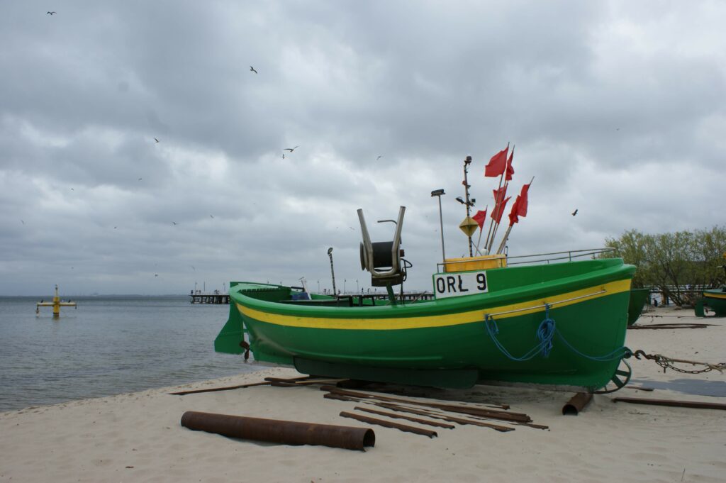 Zielony kuter rybacki ORŁ 9 z czerwonymi flagami na plaży w Gdyni Orłowie.