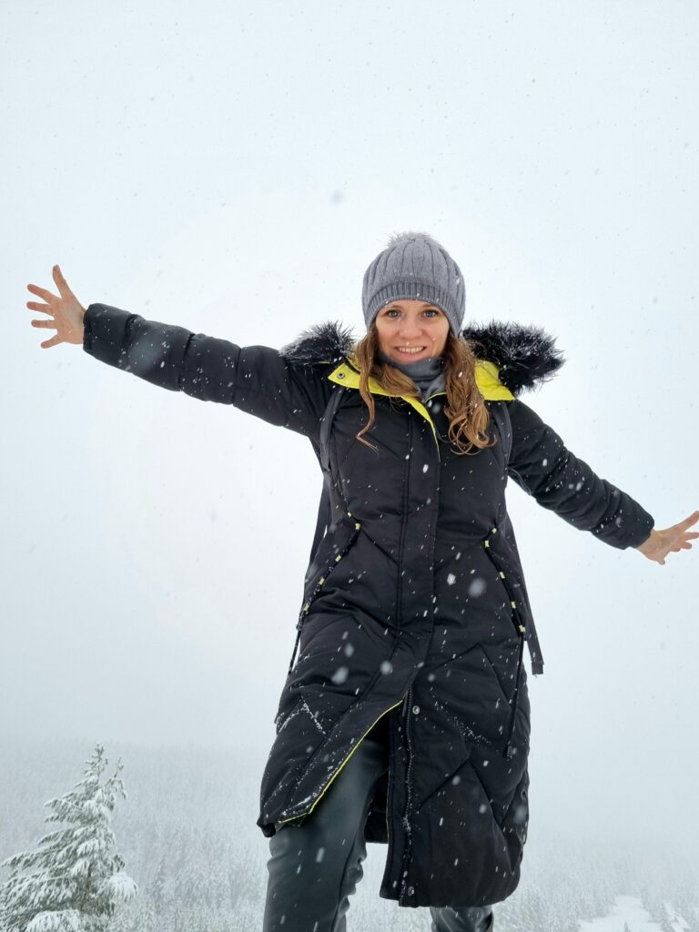 Uśmiechnięta turystka z rozłożonymi rękami na szczycie Kopieńca Wielkiego podczas mglistej pogody zimą.