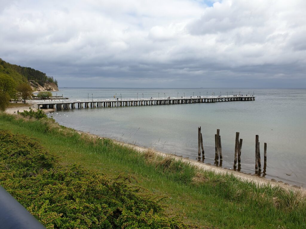 Drewniane molo w Gdyni Orłowie i Klif Orłowski w tle pod pochmurnym niebem.