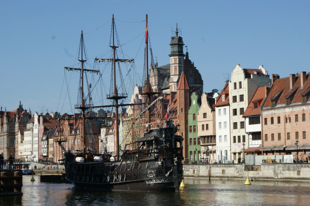 Widok na rzekę Motławę w Gdańsku z historycznym Żurawiem i cumującymi statkami wycieczkowymi.