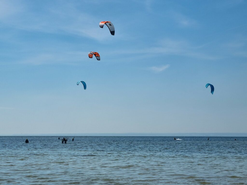 Kolorowe latawce kitesurferów na tle nieba nad płytkimi wodami Zatoki Puckiej w Jastarni.