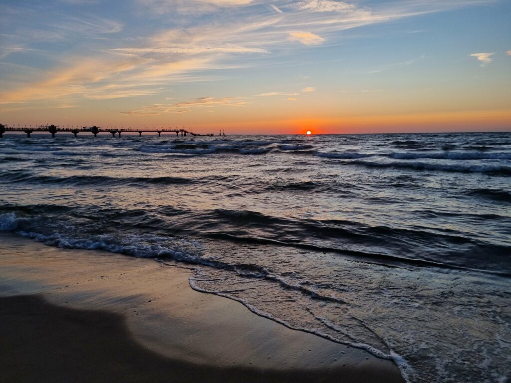 Pomarańczowe niebo i słońce chowające się za horyzontem w Międzyzdrojach.