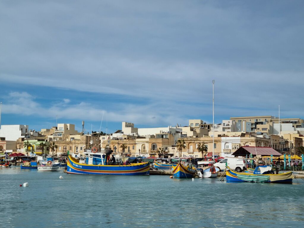 Malowniczy port w Marsaxlokk na Malcie z dziesiątkami tradycyjnych, kolorowych łodzi luzzu na wodzie.