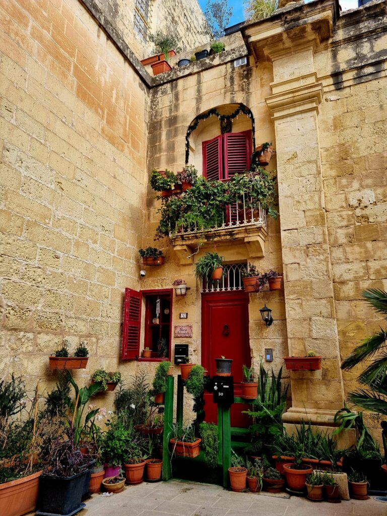 Wąska, cicha uliczka w Mdinie z charakterystycznymi piaskowymi murami i ozdobnymi drzwiami.