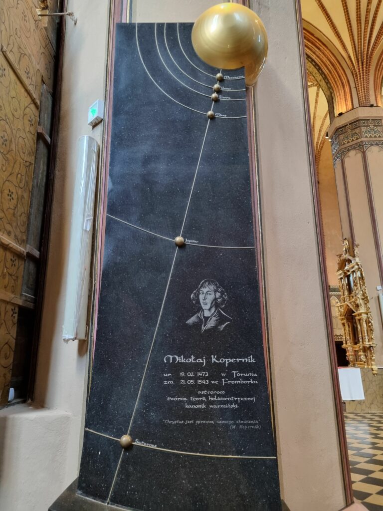 Nowoczesny, granitowy nagrobek w Katedrze oraz monumentalny pomnik Mikołaja Kopernika u stóp Wzgórza Katedralnego we Fromborku.