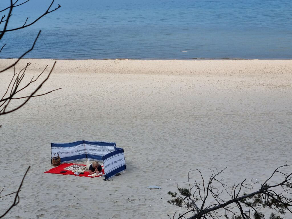 Szeroki widok na piaszczystą plażę i błękitne Morze Bałtyckie z delikatnymi falami pod bezchmurnym niebem.