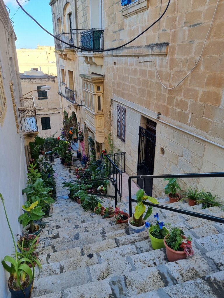 Wąskie, klimatyczne uliczki w Birgu (Vittoriosa) ozdobione kwiatami i tradycyjnymi maltańskimi balkonami.