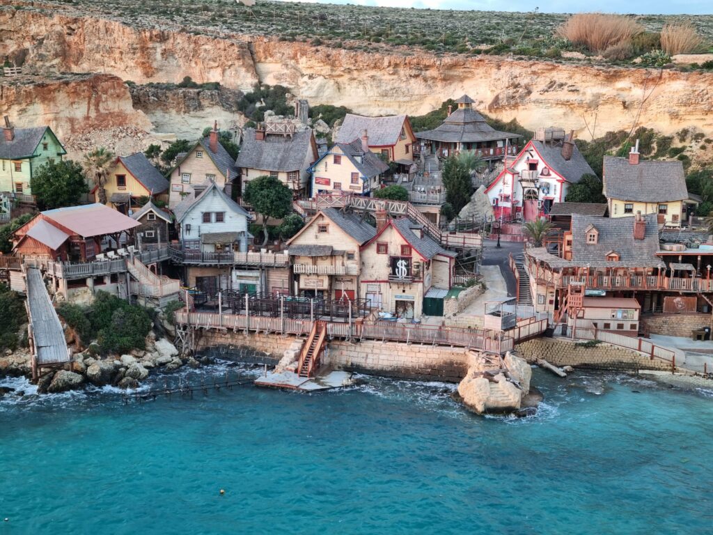 Panorama kolorowej wioski Popeye Village w zatoce Anchor Bay widziana z wysokiego klifu na Malcie.