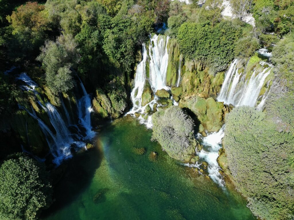 Perspektywa z drona ukazuje całą potęgę wodospadów Kravica i ich niezwykłe położenie w sercu zielonej oazy.