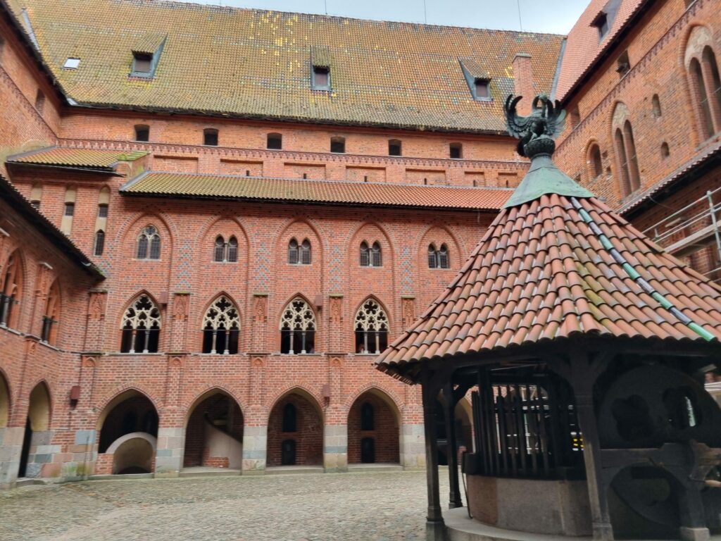 Wewnętrzny dziedziniec Zamku Krzyżackiego w Malborku otoczony monumentalnymi, gotyckimi murami i krużgankami