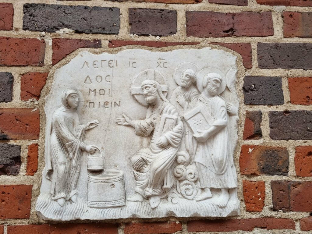 Kamienna płaskorzeźba wmurowana w ceglaną ścianę Zamku w Malborku, przedstawiająca Jezusa i Samarytankę przy studni.