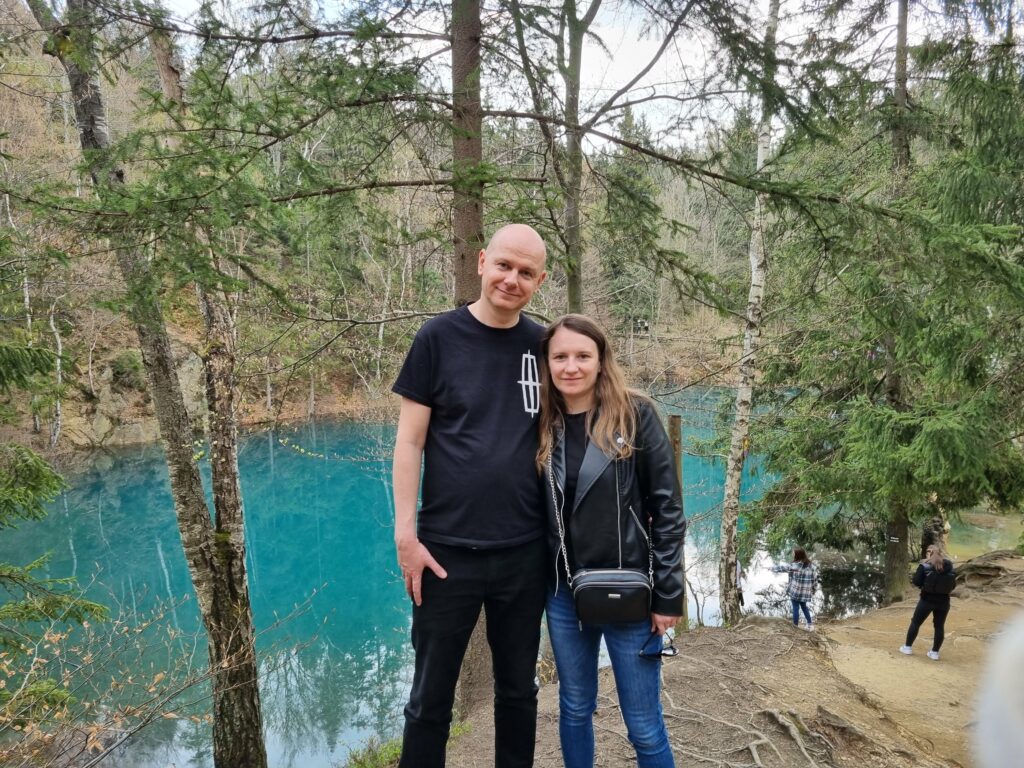 Turyści spacerujący i odpoczywający na drewnianych kładkach nad brzegiem lazurowego Błękitnego Jeziorka w Rudawach Janowickich.