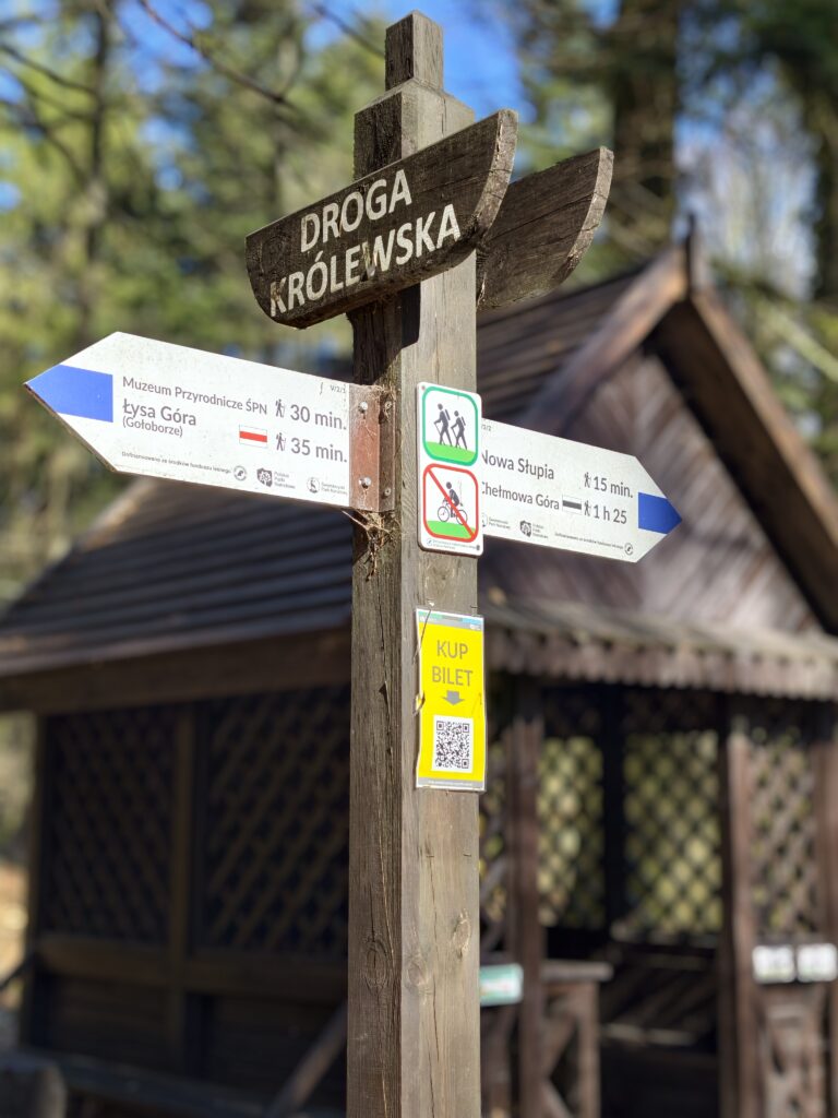 Drewniany drogowskaz PTTK na niebieskim szlakiem informujący o czasie przejścia z Nowej Słupi na Święty Krzyż.