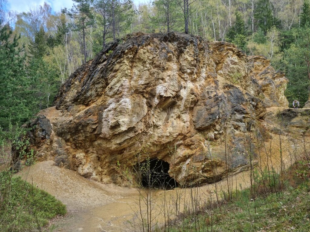 Niewielka jaskinia i wydrążona w rdzawej skale dawna sztolnia kopalni pirytu przy Purpurowym Jeziorku w Rudawach Janowickich.