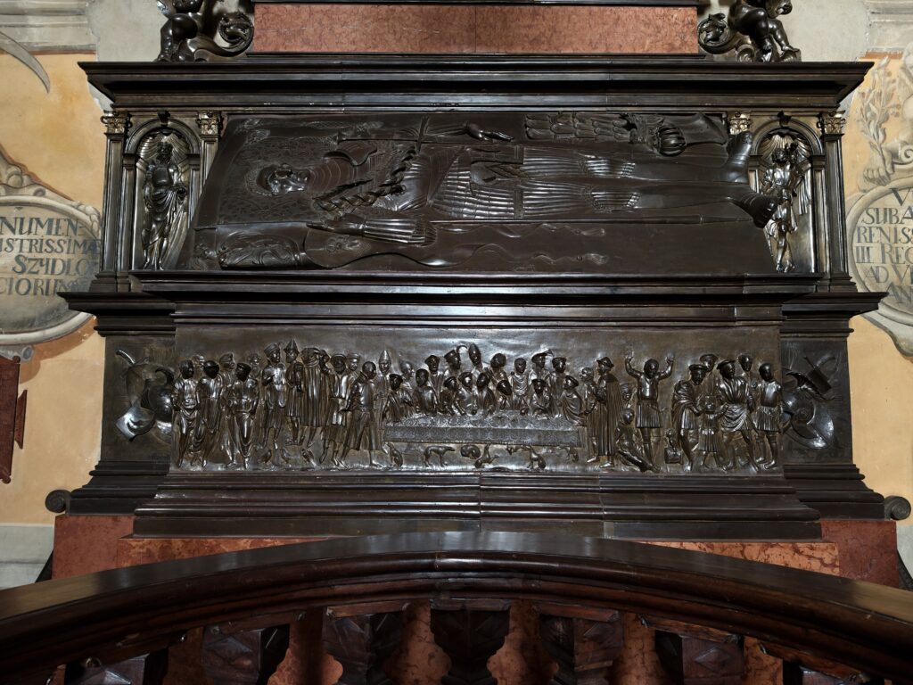 Zbliżenie na renesansową płaskorzeźbę z brązu, znaną jako Lament Opatowski, przedstawiającą opłakujące postacie.