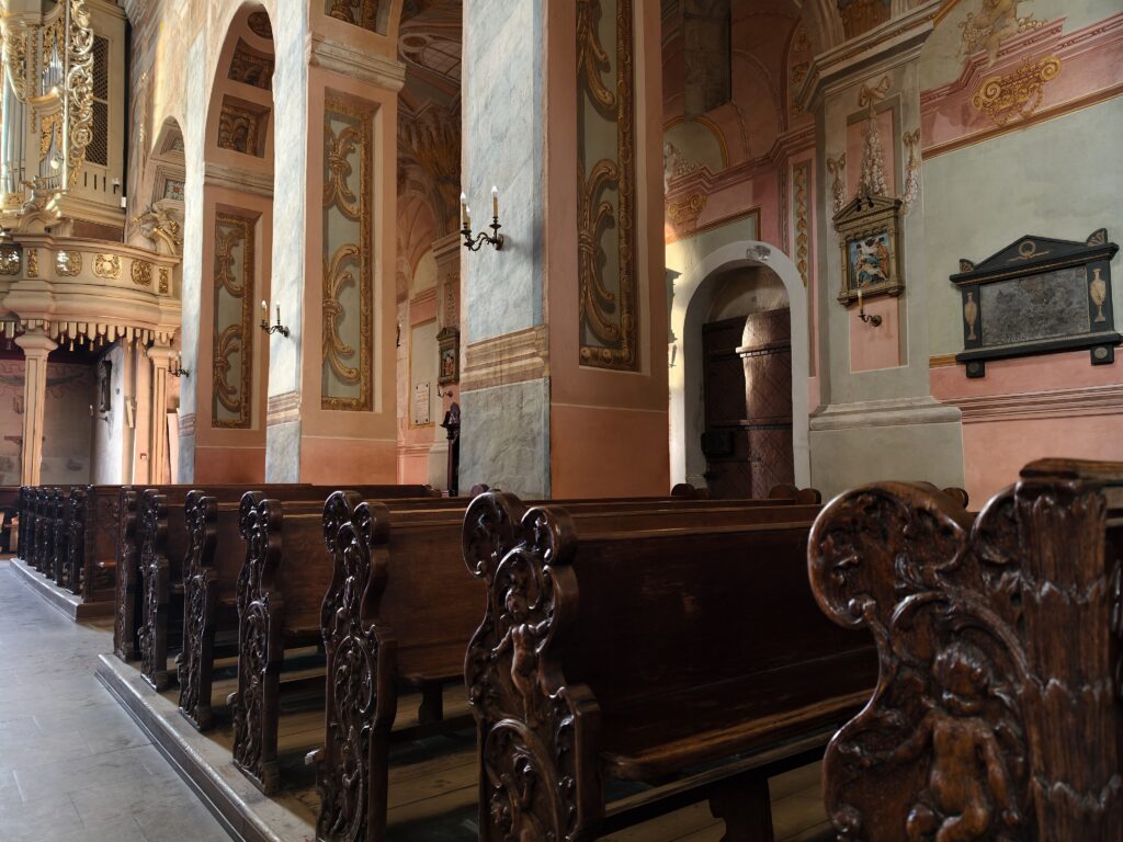 Zbliżenie na bogato zdobione, drewniane ławy z rzeźbionymi detalami w nawie głównej Kolegiaty św. Marcina w Opatowie.