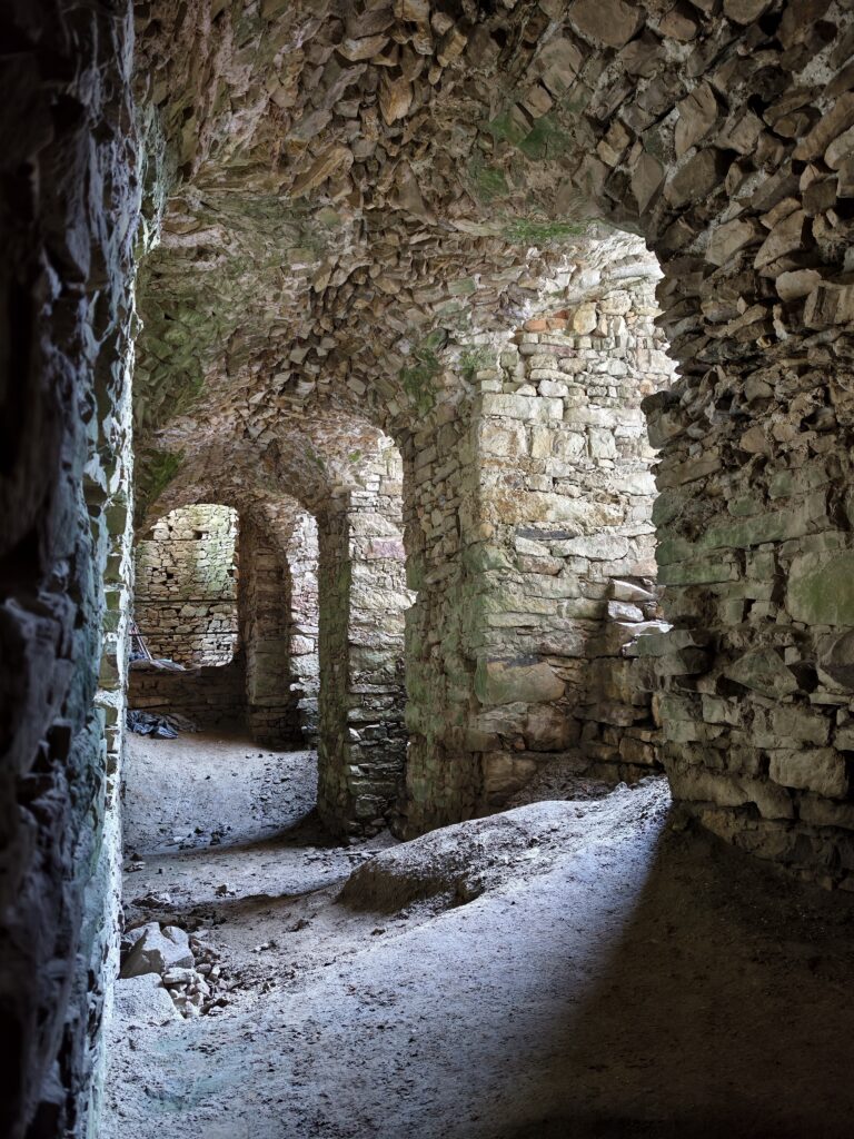 Perspektywa długiego, kamiennego korytarza w podziemiach Zamku Krzyżtopór z historycznymi sklepieniami kolebkowymi.