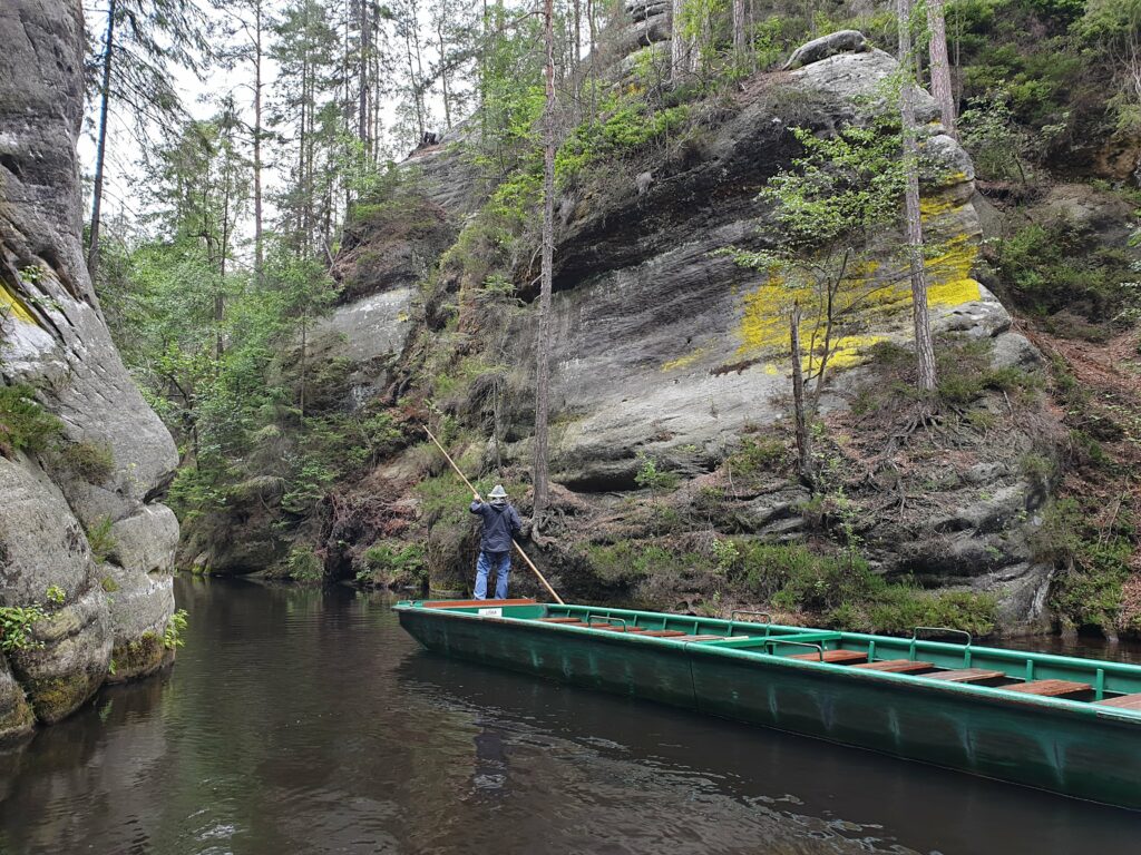Flisak płynący drewnianą łódką po małym górskim jeziorku niedaleko Wielkiego Wodospadu w Skalnym Mieście Adrspach w Czechach. Rejs łódeczką Adršpach