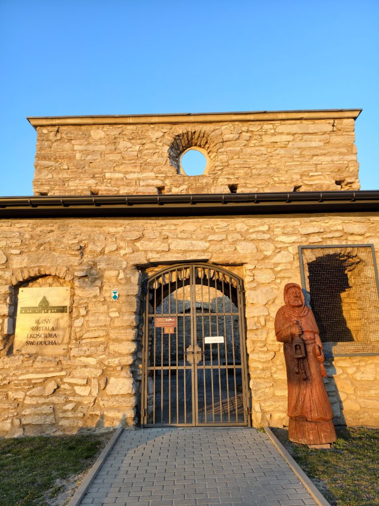 Pozostałości kamiennych murów zrujnowanego kościoła i szpitala Ducha Świętego w Szydłowie w otoczeniu drzew.