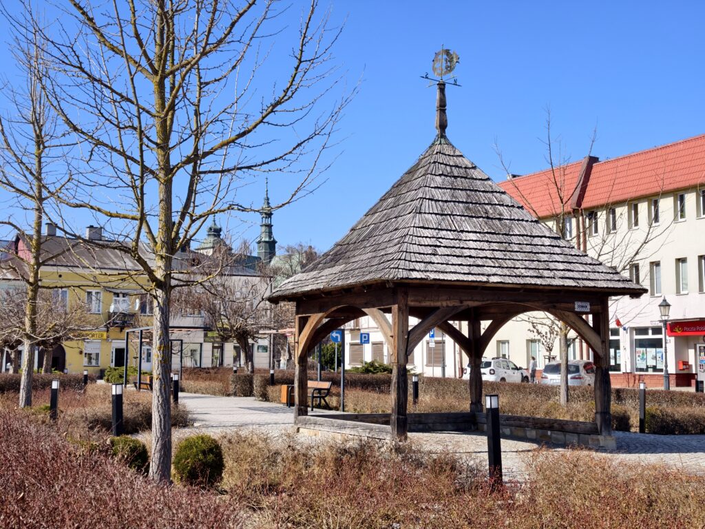 Zbliżenie na centralną płytę Rynku w Opatowie z widocznym historycznym brukiem oraz detalami architektury zabytkowych kamienic w tle.