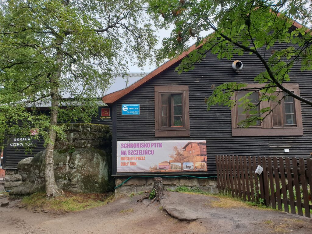 Budynek Schroniska PTTK na Szczelińcu Wielkim w Górach Stołowych widziany z zewnątrz na tle skał.