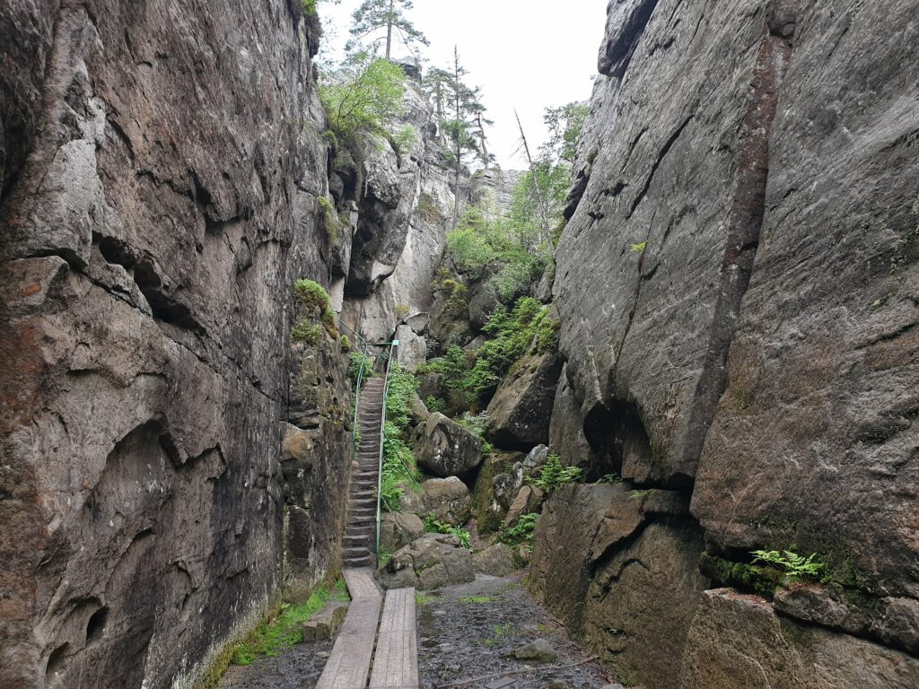 Wąskie metalowe schody prowadzące przez labirynt skalny wśród wysokich formacji piaskowca na szczycie Szczelińca Wielkiego.