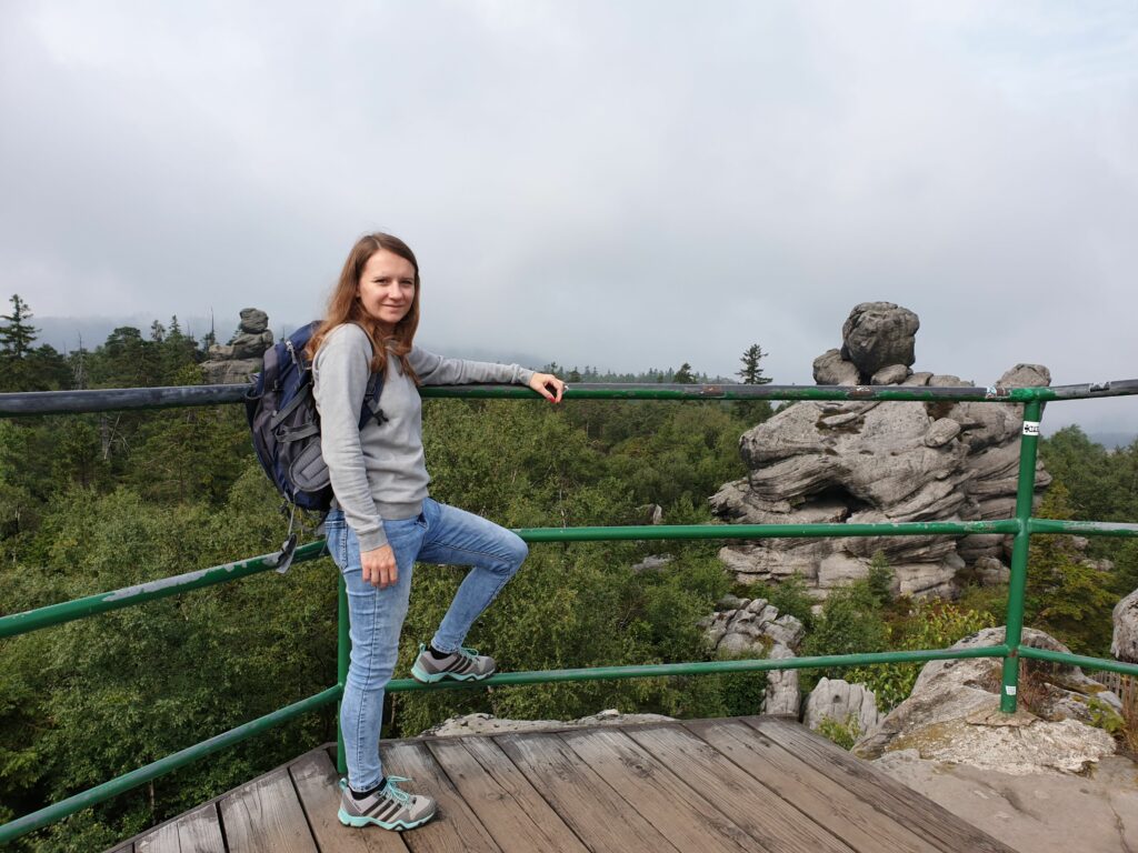 Kobieta stojąca na tarasie widokowym przy Schronisku PTTK na Szczelińcu Wielkim, patrząca na rozległą panoramę Sudetów i czeskie Góry Stołowe.