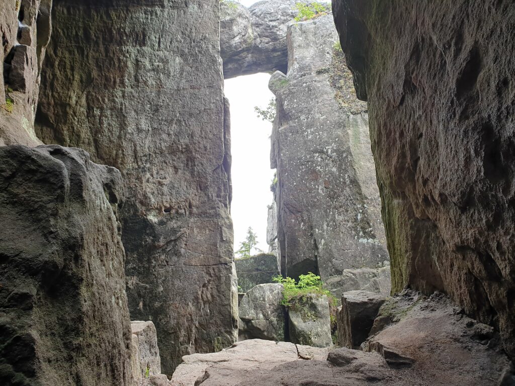 Widok z wąskiej, mrocznej szczeliny (w stylu Piekiełka) w labiryncie skalnym, ze światłem wpadającym przez skalne okno na Szczelińcu Wielkim.
